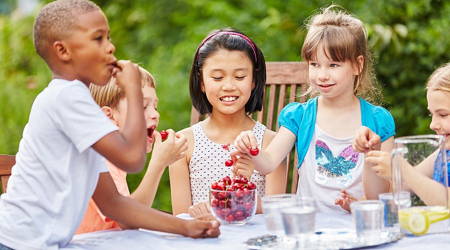 Kinder, die zusammen an einem Tisch sitzen und Kirschen essen.