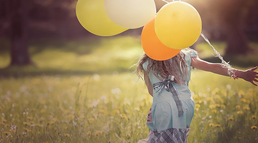 Ein glücklichen Mädchen rennt über eine Wiese mit bunten Luftballons