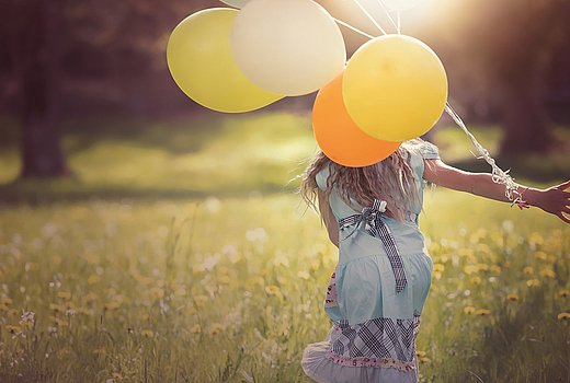 Ein glücklichen Mädchen rennt über eine Wiese mit bunten Luftballons