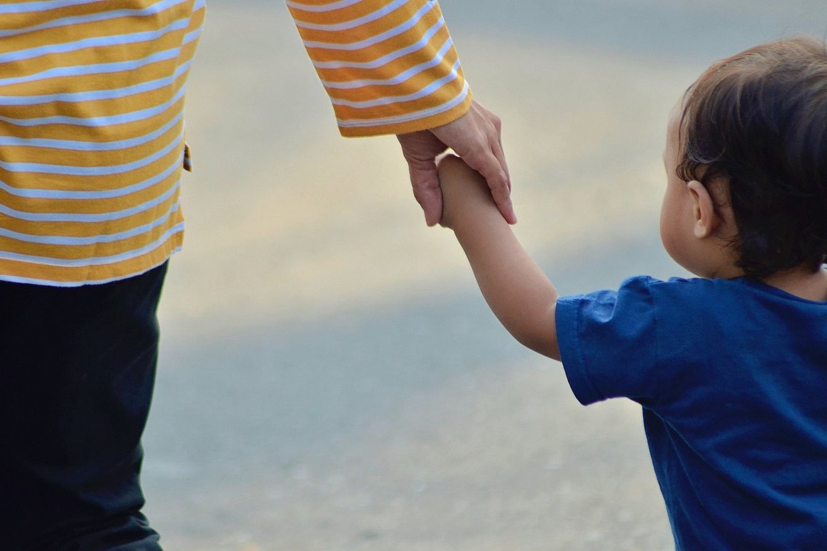 Ein Kleinkind geht an der Hand eines Erwachsenen.