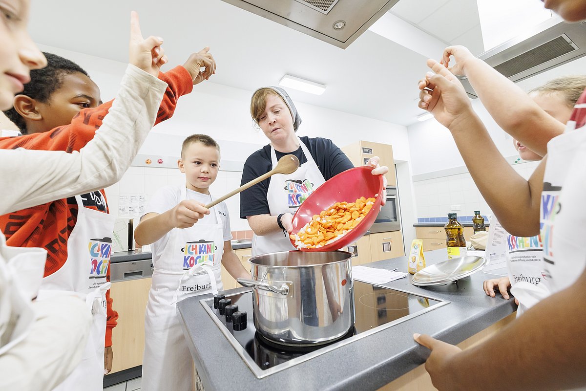 Kinder kochen gemeinsam mit einer Fachkraft in der Küche einen Eintopf. 