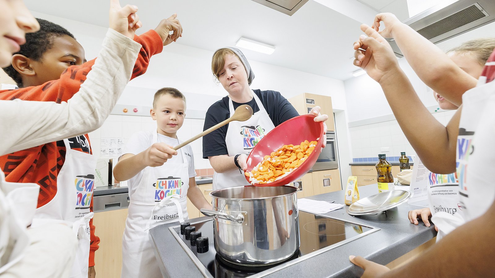 Kinder kochen gemeinsam mit einer Fachkraft in der Küche einen Eintopf. 