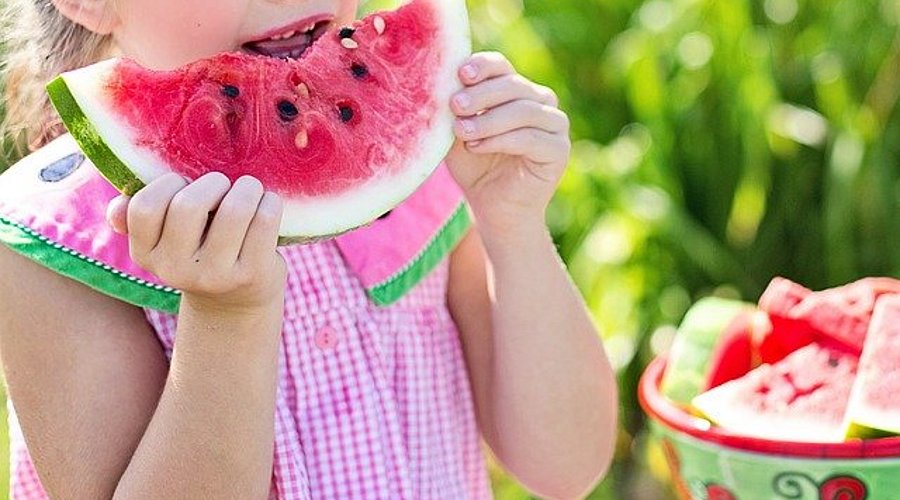 Schulmädchen beißt in eine Scheibe einer Wassermelone. 