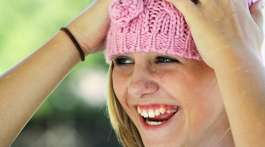 Ein jugendliches Mädchen hat eine rosa Strickmütze auf und greift sich mit den Händen an den Kopf. 