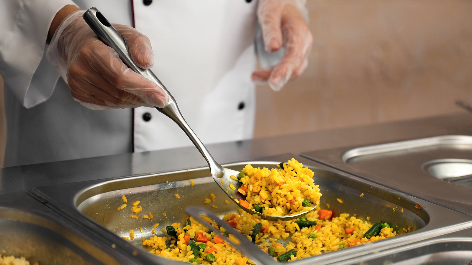 Ein Küchenmitarbeiter portioniert Essen an der Ausgabe einer Mensa