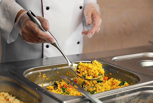 Ein Küchenmitarbeiter portioniert Essen an der Ausgabe einer Mensa