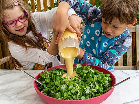 Kinder bereiten gemeinsam Salat mit Dressing vor