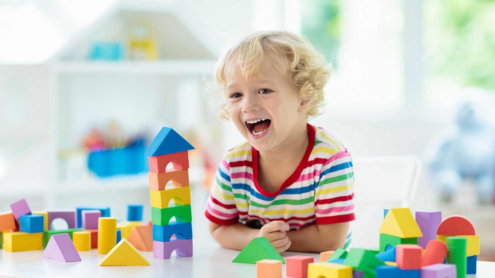 Kind spielt mit bunten Holzbauklötzchen und lacht 