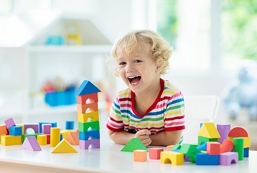 Kind spielt mit bunten Holzbauklötzchen und lacht 