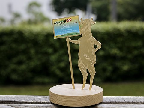 Trophäe des Schulwettbewerbs Echt kuh-l: Eine stehende Kuh hält ein Schild.