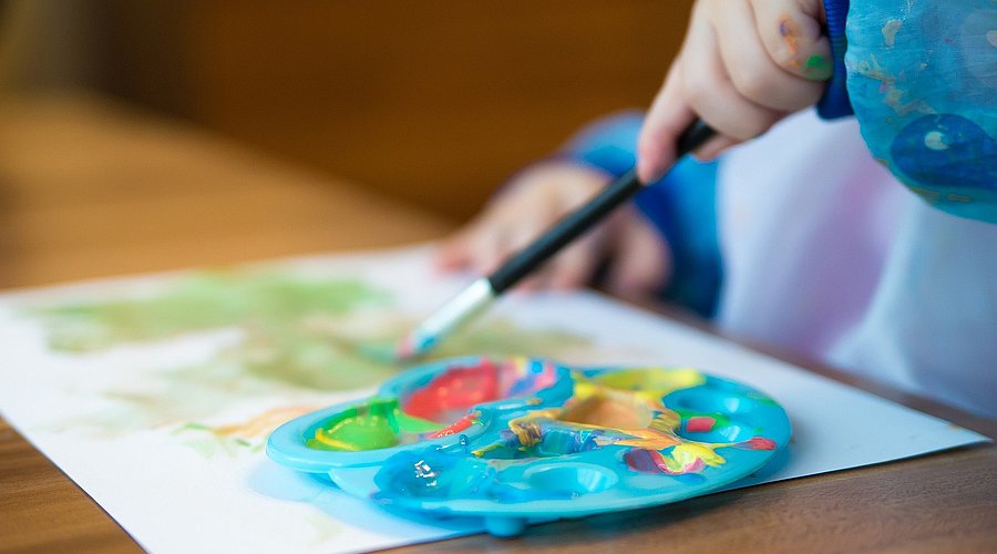 Kind sitzt am Tisch und malt mit Wasserfarben. 