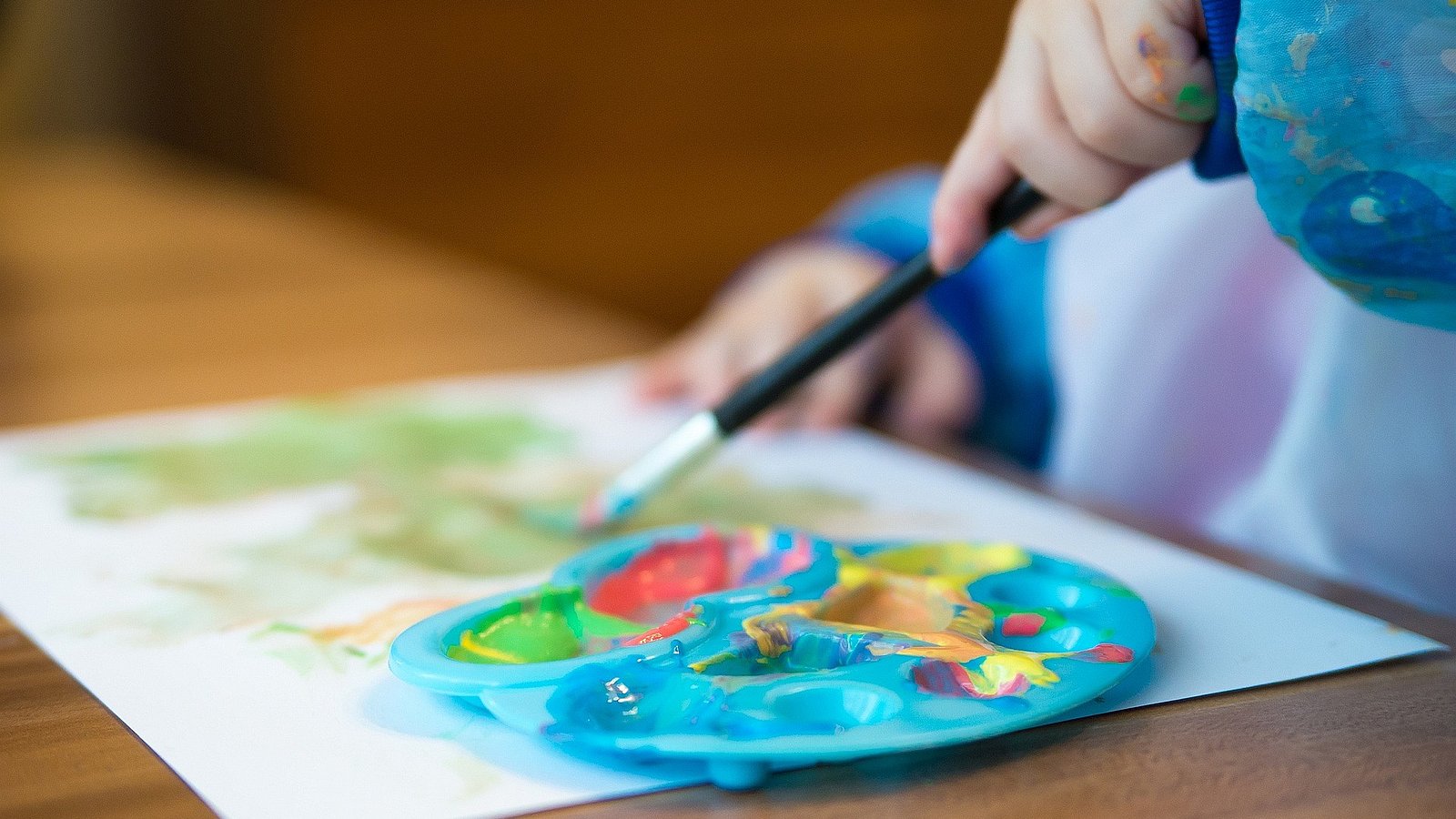 Kind sitzt am Tisch und malt mit Wasserfarben. 