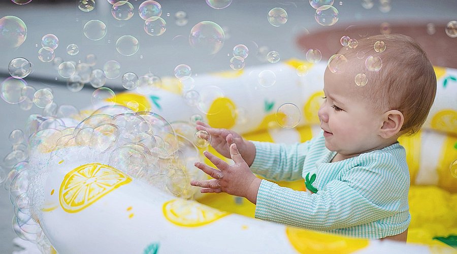 Kleinkind sitzt im Planschbecken und spielt mit Seifenblasen.