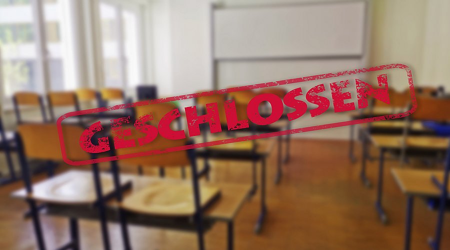 In einem Klassenzimmer sind alle Stühle hochgestellt. Quer über das Bild verläuft ein Banner mit dem Wort "Geschlossen". 