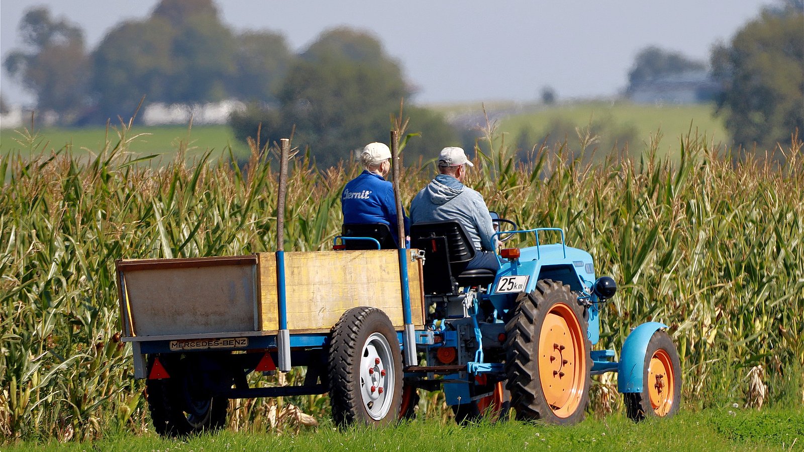 Zwei Landwirt*innen sitzen auf einem Traktor und fahren über das Feld. 
