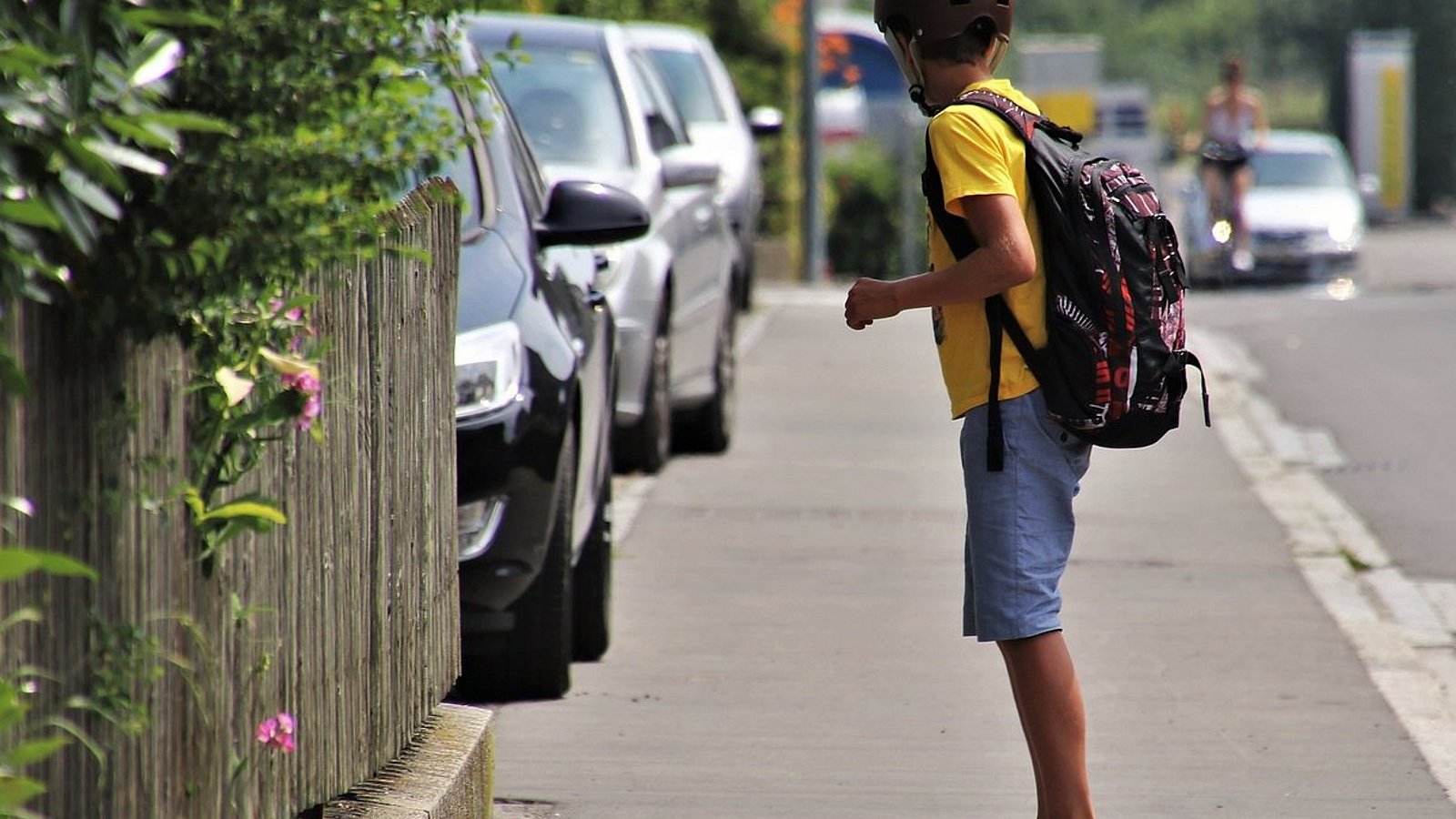 Ein Junge fährt auf einem Skateboard über den Bürgersteig. Er trägt kurze Hosen und Helm.