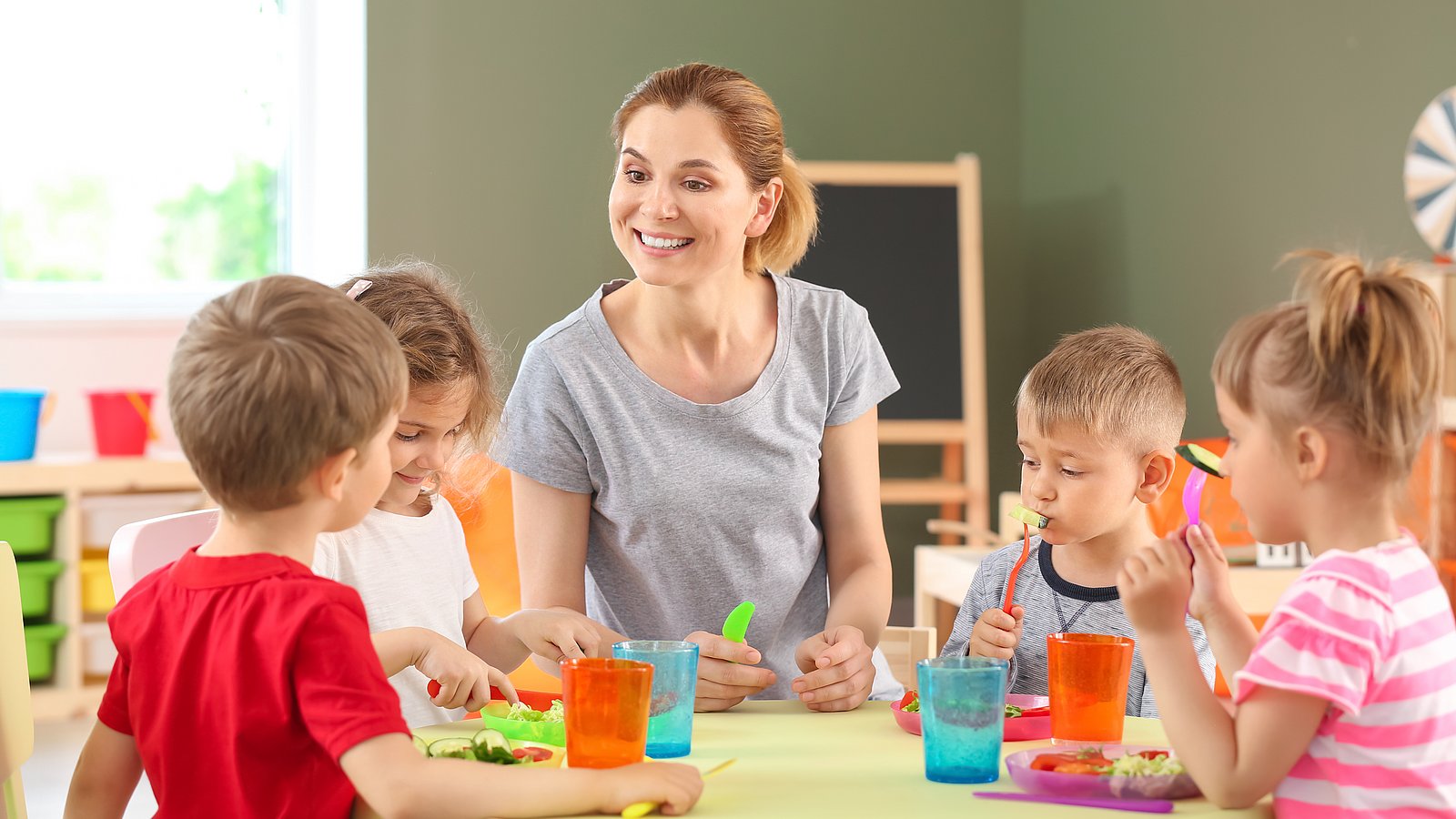 Kinder sitzen um einen Tisch mit buntem Geschirr