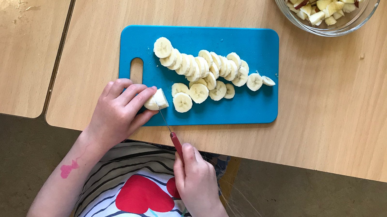 Kind schneidet in einer Kita eine Banane in Stücke. 