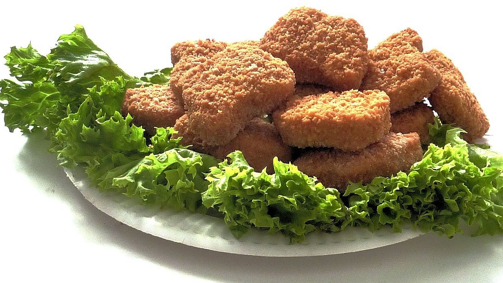 Auf einem weißen Teller liegen Salatblätter und darauf frittierte und panierte Chicken Nuggets.