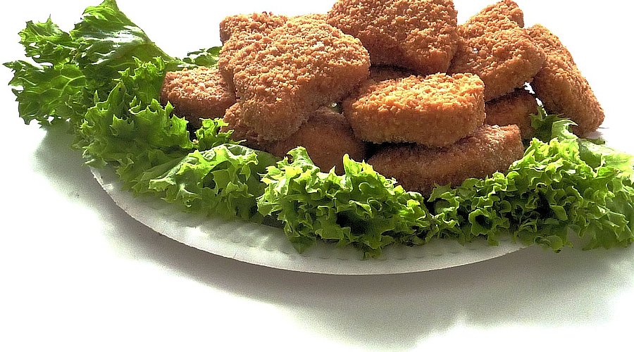 Auf einem weißen Teller liegen Salatblätter und darauf frittierte und panierte Chicken Nuggets.