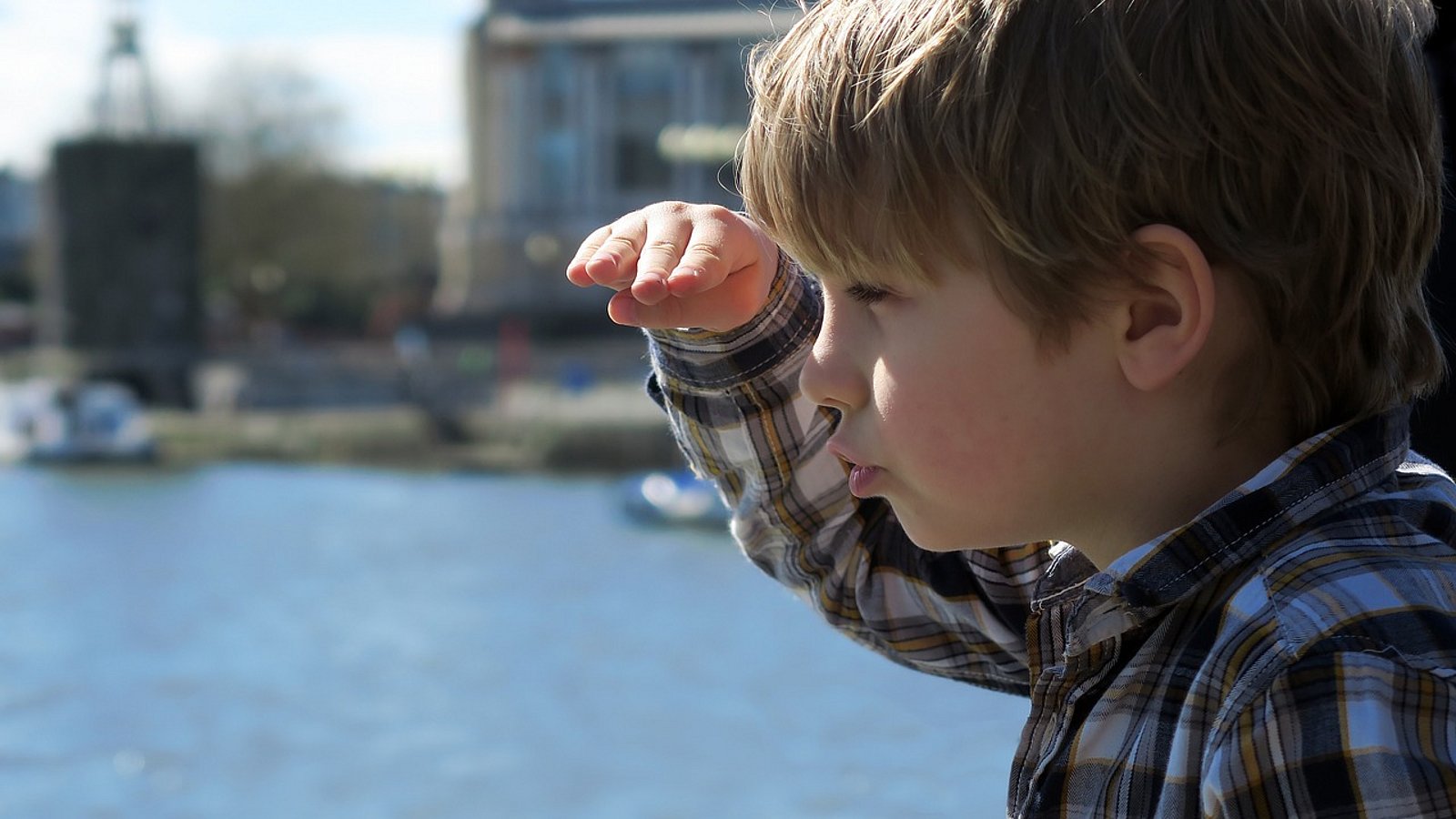 Ein Junge schaut in die Ferne und legt dabei die Hand über die Augen. Im Hintergrund ein See oder das Meer.