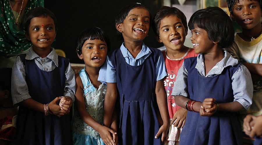 Indische Grundschulkinder stehen in Schuluniform in einer Gruppe zusammen und lachen.