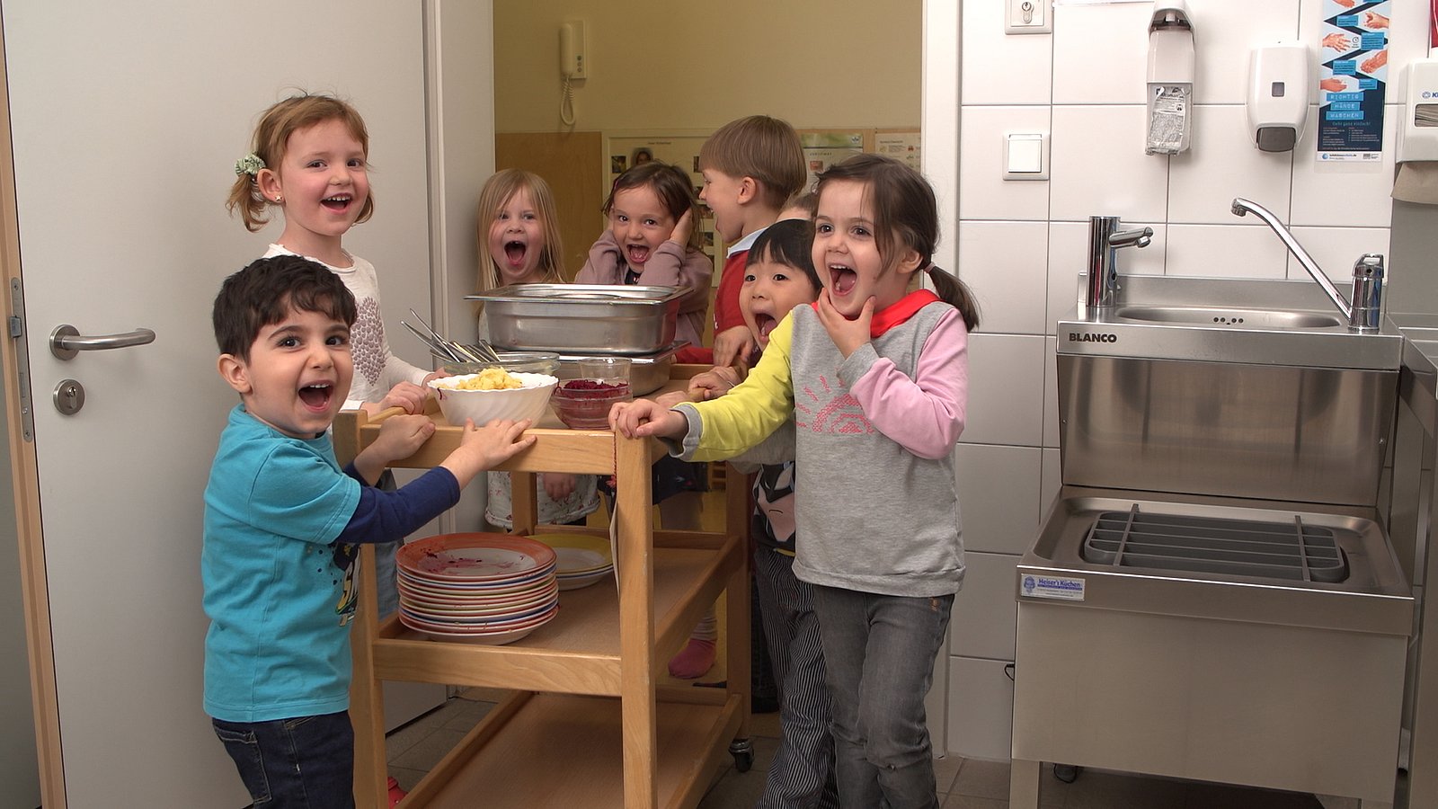 Kita-Kinder bringen schmutziges Geschirr nach dem Essen in die Küche.