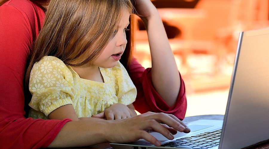 Eine Frau sitzt mit ihrer Tochter vor einem Laptop. Beide haben die Hände auf der Tastatur.