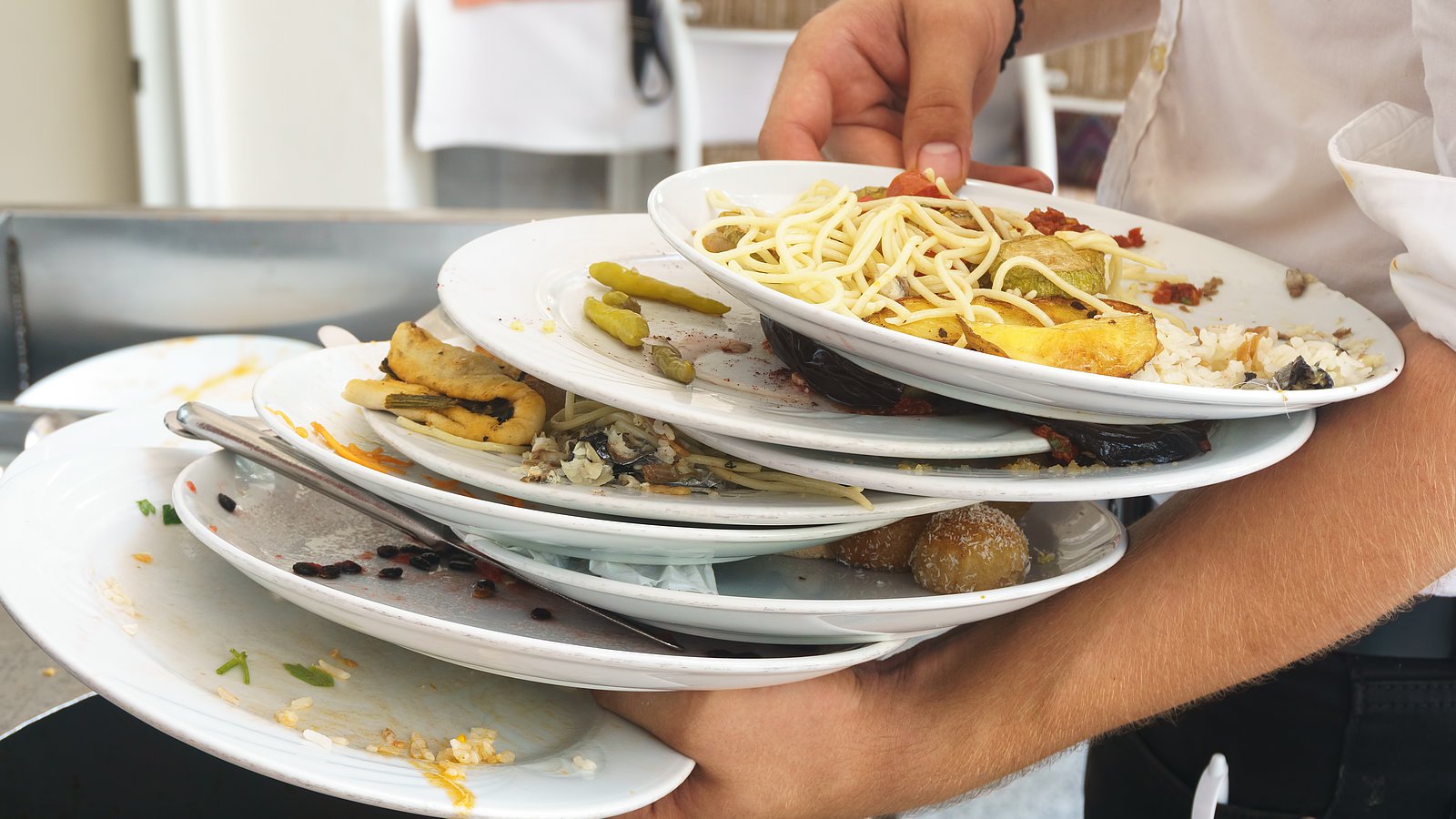 Kellner hält viele gestapelte Teller mit Essensresten in der Hand.
