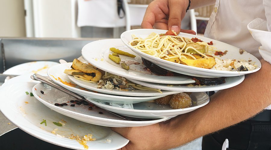 Kellner hält viele gestapelte Teller mit Essensresten in der Hand.