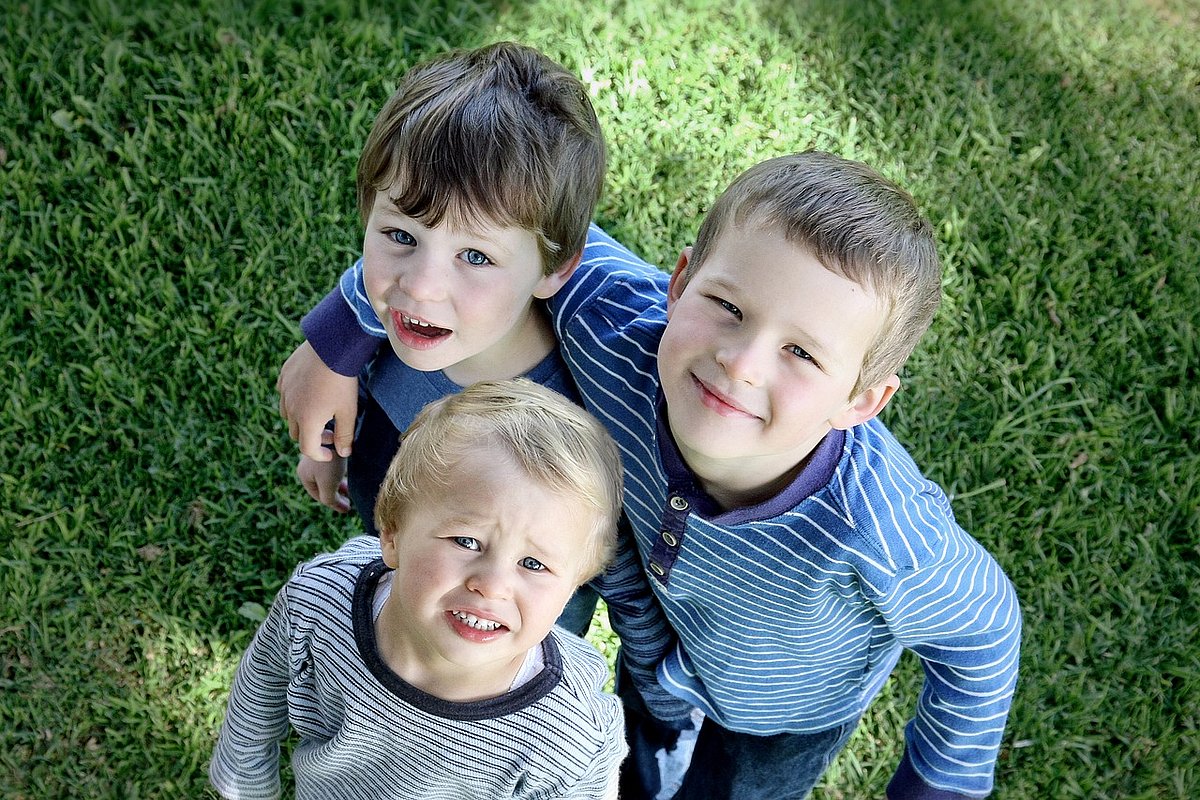 Drei Jungen verschiendenen Alters stehen eng aneinander auf einem Rasen und blicken nach oben.