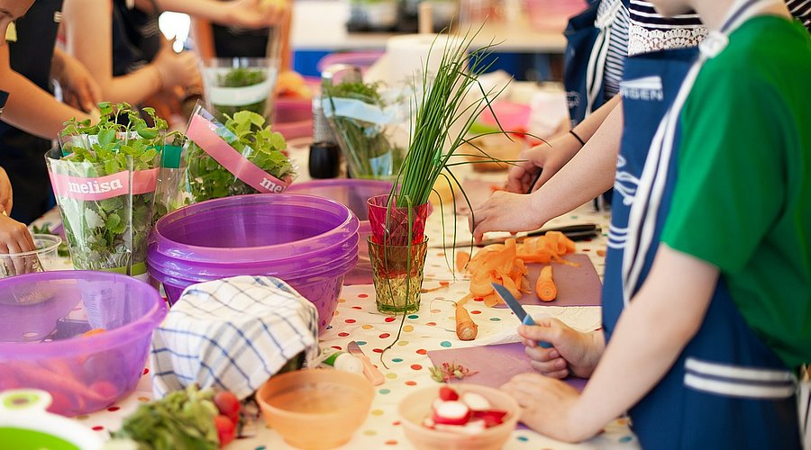 Schulkinder stehen an einem Tisch und schneiden Gemüse.