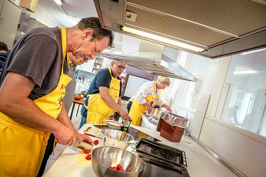 Workshop-Teilnehmende arbeiten im kochpraktischen Teil in einer Küche.