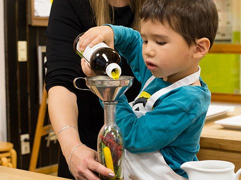 Kind befüllt Flasche mit Öl mit Hilfe einer Erzieherin.
