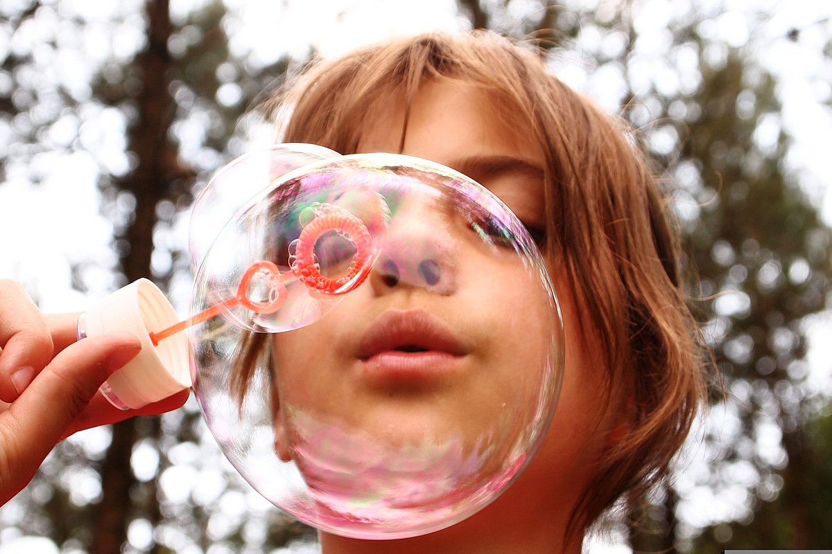 Ein Mädchen pustet eine große Seifenblase. 