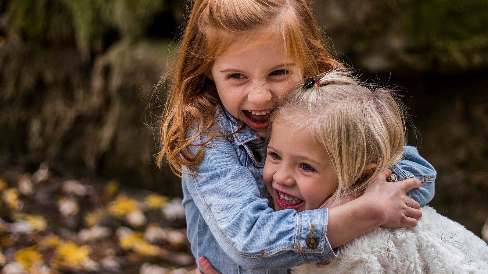 Zwei kleine Mädchen umarmen sich innig und lachen.