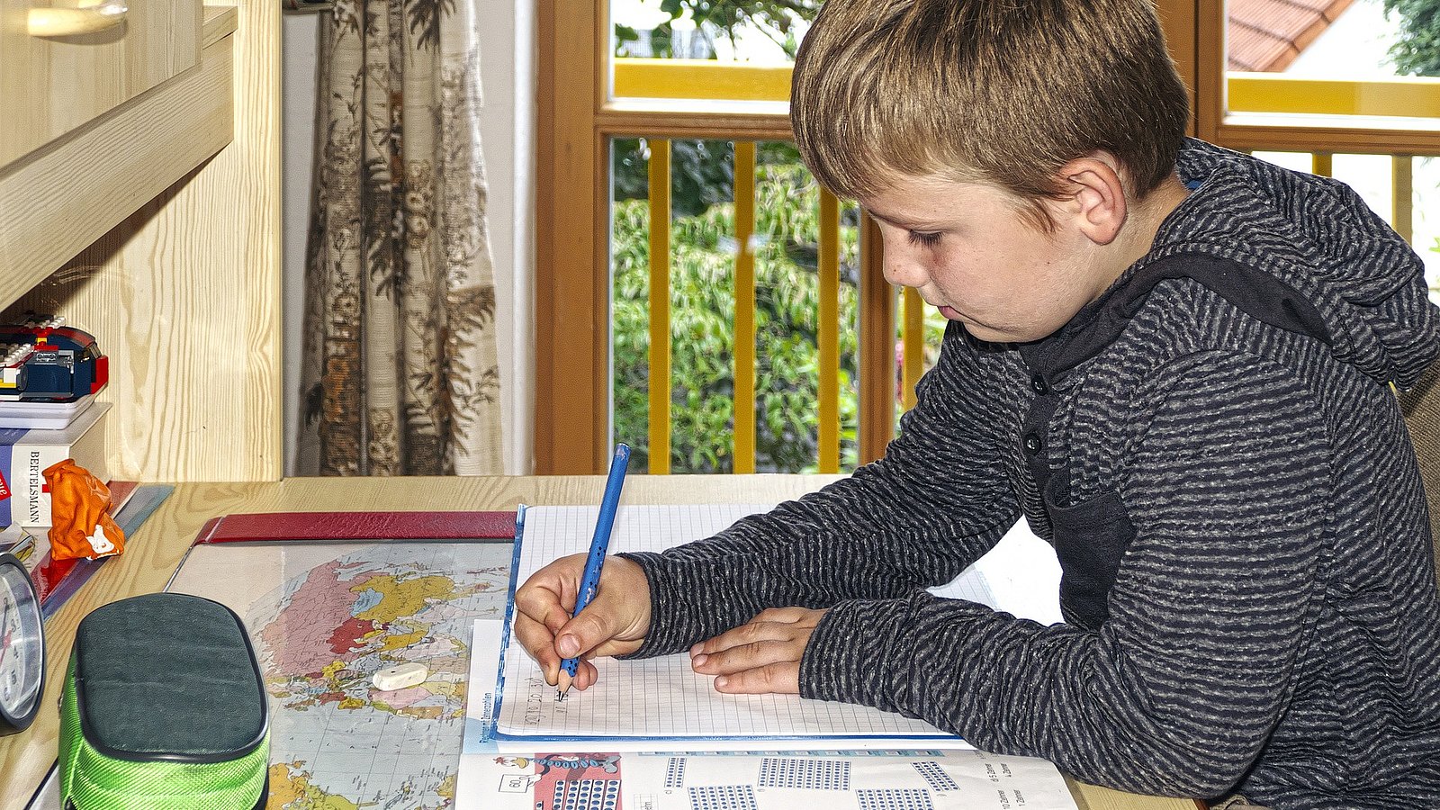 Ein jugendlicher Junge sitzt an seinem Schreibtisch und macht seine Hausaufgaben.