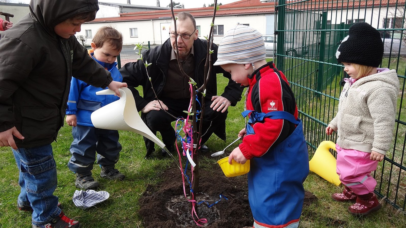 Kindergartenkinder pflanzen gemeinsam mit einem Erzieher einen Baum