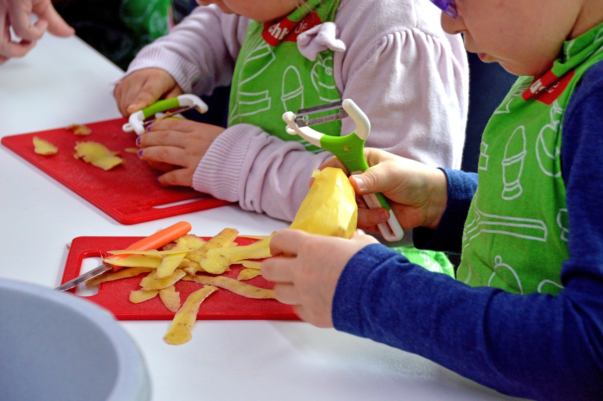 Kinder in Kochschürzen schälen Kartoffeln